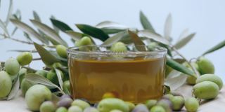 成熟的绿色橄榄倒入透明的碗中与天然橄榄油在慢动作，橄榄油工业和生产的健康有机产品从天然种植园，农业的概念