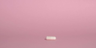 药丸落在粉红色的背景上。白色药片或维生素慢慢地涌进来。药理学、药品、补充剂、治疗和保健理念。
