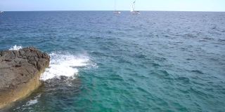 海浪拍打着岩石海岸，以航行的船只为背景