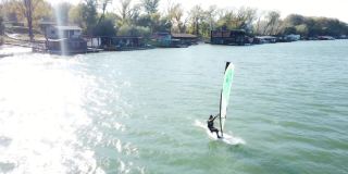 风帆冲浪者在有风的日子在城市的河边冲浪。无人机的画面。