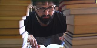 一个留着胡子、戴着眼镜的男人在一堆书中寻找信息。