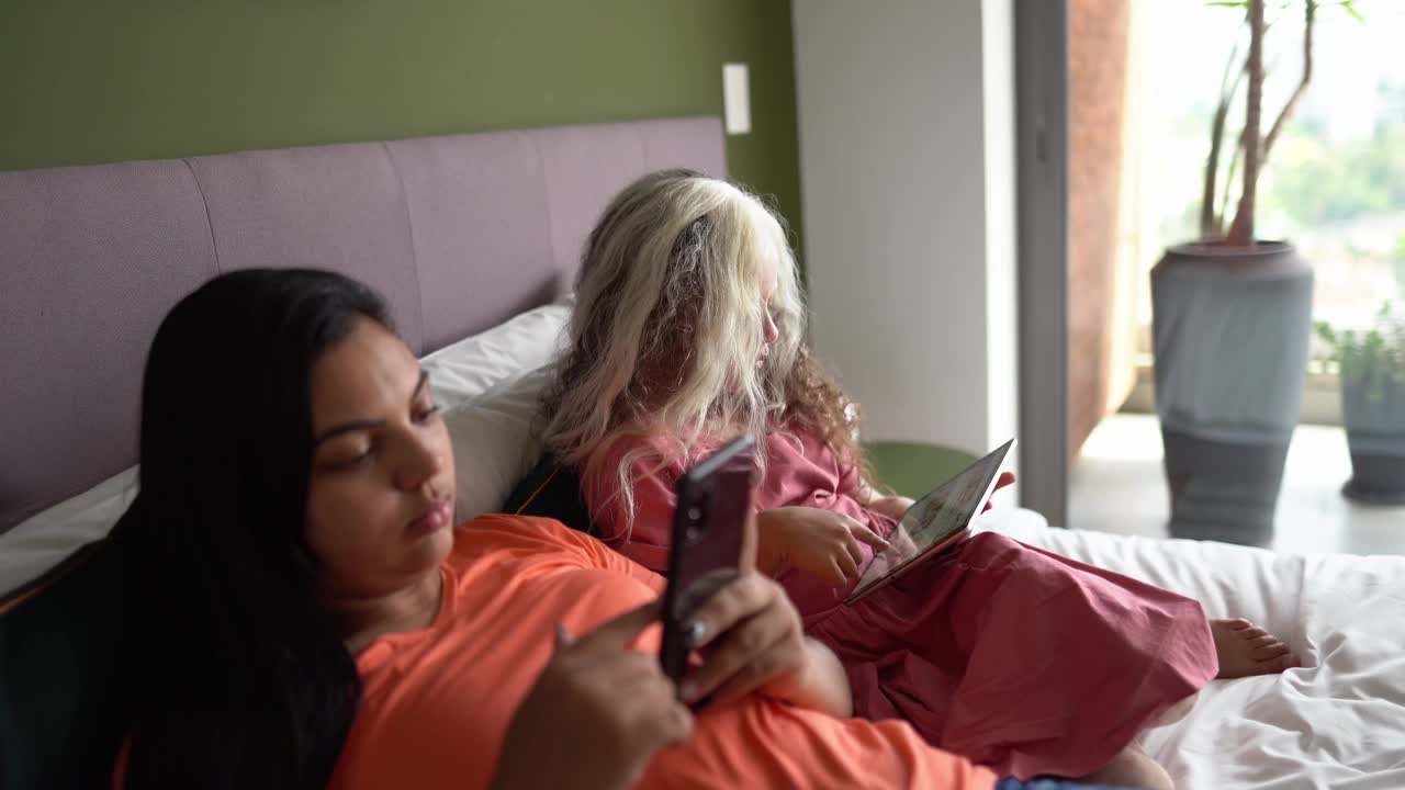 母亲在家里使用智能手机，女儿在家里使用数字平板电脑——患有花斑症的女孩