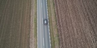 这辆车正行驶在穿过田野的道路上，无人机拍摄了航拍画面。秋天的时候在柏油路上，摄影机跟在车的后面。