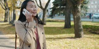 多莉拍摄的亚洲女企业家走在外面，讲移动电话
