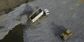 强力自卸车卸下碎石和推土机，将花岗岩碎石压平地基，供建筑使用