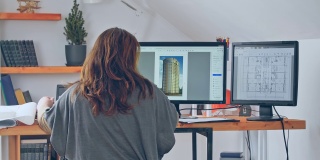 在一个高层建筑的项目中，一个女人用笔记本电脑和两个额外的显示器工作的背影。使用远程方案在家工作的概念。检疫