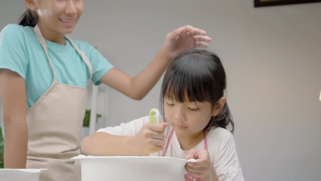 快乐的亚洲孩子在家里学习做饼干，女孩在搅拌碗中打谷面团。