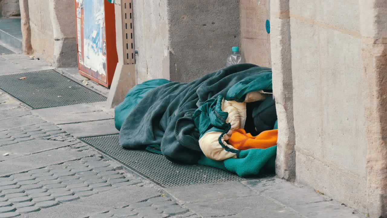 德国纽伦堡- 2019年12月10日:冬天，一名无家可归的贫穷乞丐躺在城市街道上的睡袋里乞求施舍