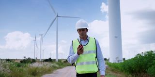 亚洲男性工程师在视察风电场、清洁能源概念、可再生能源、拯救世界时使用无线电发送工作指令。