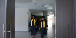 一群快乐的学生穿着学位帽和毕业礼服，笑容满面地走进毕业典礼