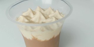 用塑料杯装掼奶油和巧克力的甜点。女性用茶匙将奶油顶部移除