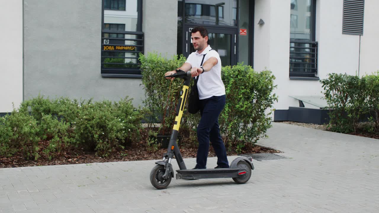 商人与公文包滚动电动滑板车在街道人行道。在夏天，男人在城市人行道上滚动电动滑板车。