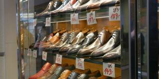 鞋店橱窗里的货架上摆放着各种颜色的经典皮革男鞋，上面还贴着价格标签