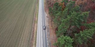 这辆车正行驶在穿过田野的道路上，无人机拍摄了航拍画面。秋天的时候在柏油路上，摄影机跟在车的后面。