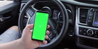 男子手滚动chromakey手机与空的绿色屏幕在车。模型触摸屏。绿色智能手机显示。