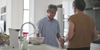 亚洲华人老年夫妇喜欢在厨房跳舞，同时在周末在家做饭