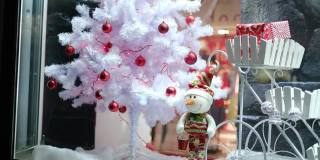 夜城的一条街上，一个零售橱窗里摆着一棵圣诞树，一个时装店的雪人橱窗里装饰着节日的彩灯和圣诞装饰品。