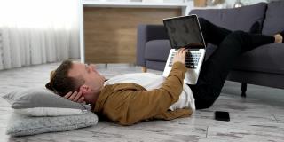 自由职业者在家工作。一个疲惫的学生躺在地板上，双腿放在沙发上，在笔记本电脑上学习。远程工作。
