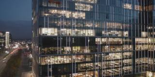 夜晚摩天大楼办公室窗户的电影鸟瞰图。摄像头在顶部移动。在一个玻璃摩天大楼的办公室窗户的特写。