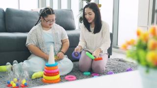 一位患有唐氏综合症的年轻女子和小女孩在家里玩耍视频素材模板下载
