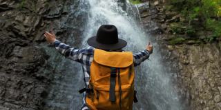 女孩旅行者戴着帽子和一个黄色的背包，而站在瀑布。生活方式的旅行概念。