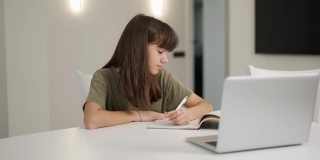 褐发少女坐在书桌前用笔记本电脑做作业