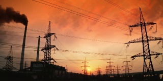 红色夕阳下，有害工厂附近的电塔。黑烟从工业管道释放到空气中。输电线路。污染环境。摄像头向下运动。