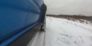 蓝色的汽车在雪地上行驶。雪飞进了相机。侧视图和车轮POV