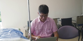 一个亚洲病人在医生的候诊室用笔记本电脑工作