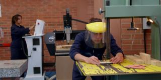 拉丁美洲的一名木工学生，用桌上的锯子切割一块木头，使用保护性的头盔面罩