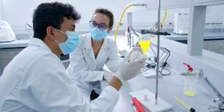 实验室的化学伙伴们戴着防护口罩和手套，一边讨论样品，一边等待反应