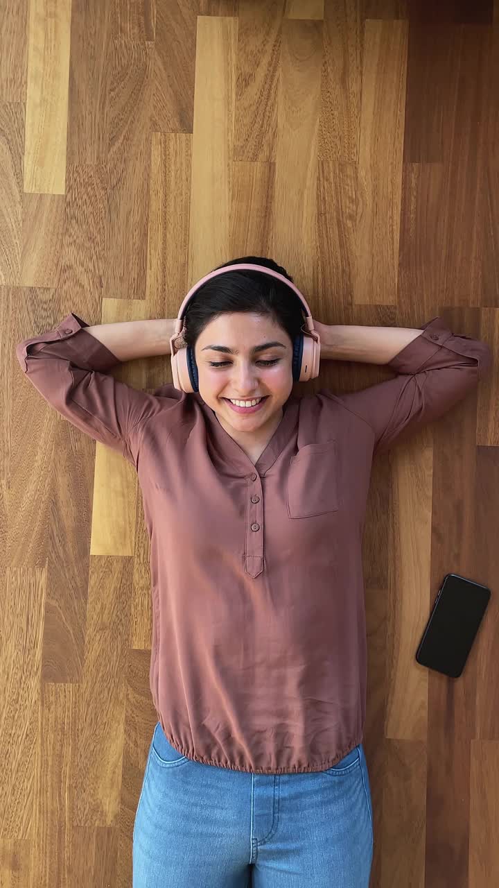 轻松的印度妇女躺在地板上通过耳机听音乐