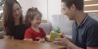 年轻的亚洲父亲给礼物盒给他的小女儿惊喜。