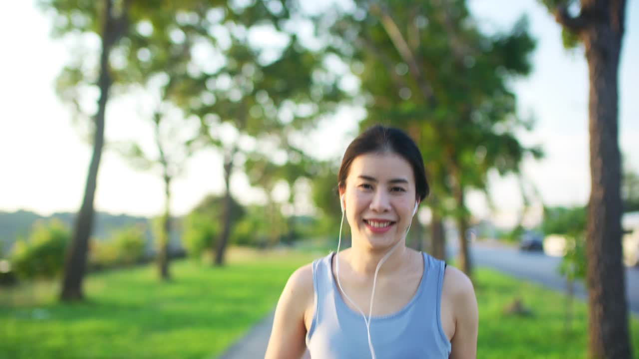 年轻女子在夕阳下在公园跑步和锻炼，微笑着面对镜头