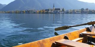 在巴伐利亚泰根塞湖风景如画的教堂的背景下，一个木船船夫拿着桨把人们带到另一边