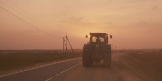 在田间播种或收割后，在日落时分行驶在乡间小路上的带大轮子的农用拖拉机