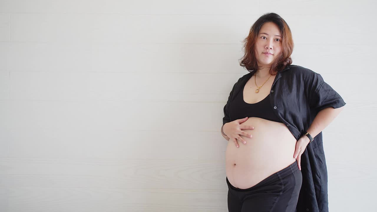 肖像吸引快乐的亚洲孕妇站着触摸她的大肚子与爱，怀孕，为人母，人们和期望的概念