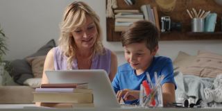 快乐的家庭在家里，妈妈和儿子玩电脑，父母和孩子在笔记本电脑上浏览互联网，小男孩的东西指向显示器