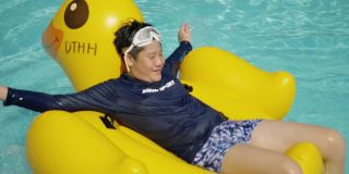 快乐的亚洲男孩放松在黄鸭橡皮筏在游泳池在假期与家人，生活理念。