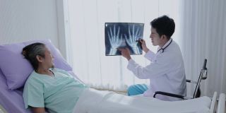亚洲男医生手持手骨x光片与男患者交谈，讲解治疗并给予鼓励。