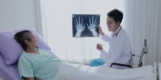 亚洲男医生手持手骨x光片与男患者交谈，讲解治疗并给予鼓励。