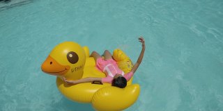 快乐的亚洲女孩放松在黄鸭橡皮筏在游泳池在假期与家人，生活理念。