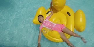 快乐的亚洲女孩放松在黄鸭橡皮筏在游泳池在假期与家人，生活理念。