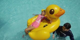 快乐的亚洲儿童在度假期间与家人在酒店或度假胜地一起在泳池中玩黄鸭橡皮艇，生活理念。