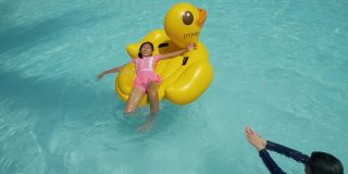 快乐的亚洲儿童在度假期间与家人在酒店或度假胜地一起在泳池中玩黄鸭橡皮艇，生活理念。