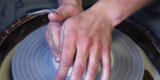 师傅的手控制着陶工学徒的手在陶工轮上的压力