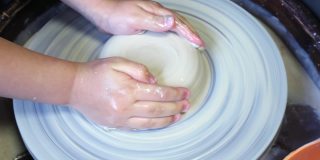 陶工大师的手在陶工轮上给学生的粘土坯增加水分