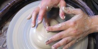 一个陶工学徒的双手正试图用陶工转盘上的一块粘土做一个杯子