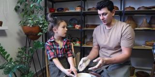 在一节陶艺大师课上，爸爸和女儿在陶艺轮上雕刻了一个陶土杯