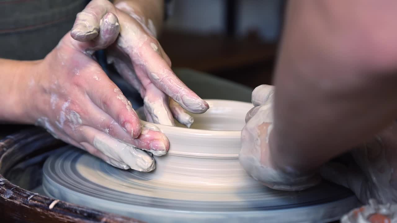 陶工师傅和他的学生用手在陶工转盘上磨平杯子的边缘